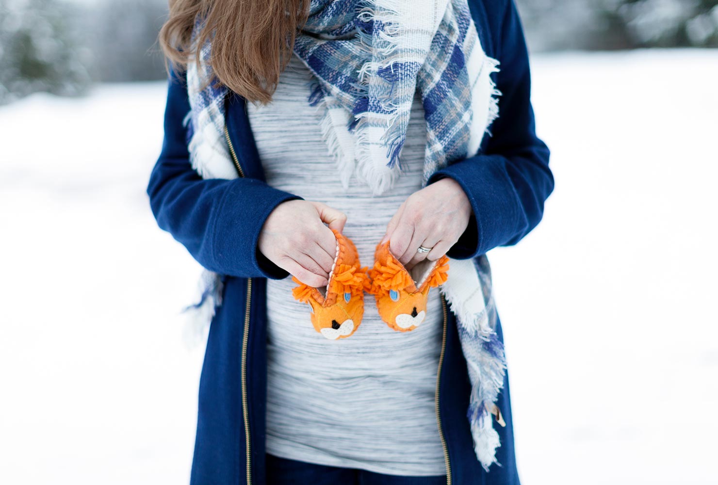 expecting mother holding up lion shoes in snow