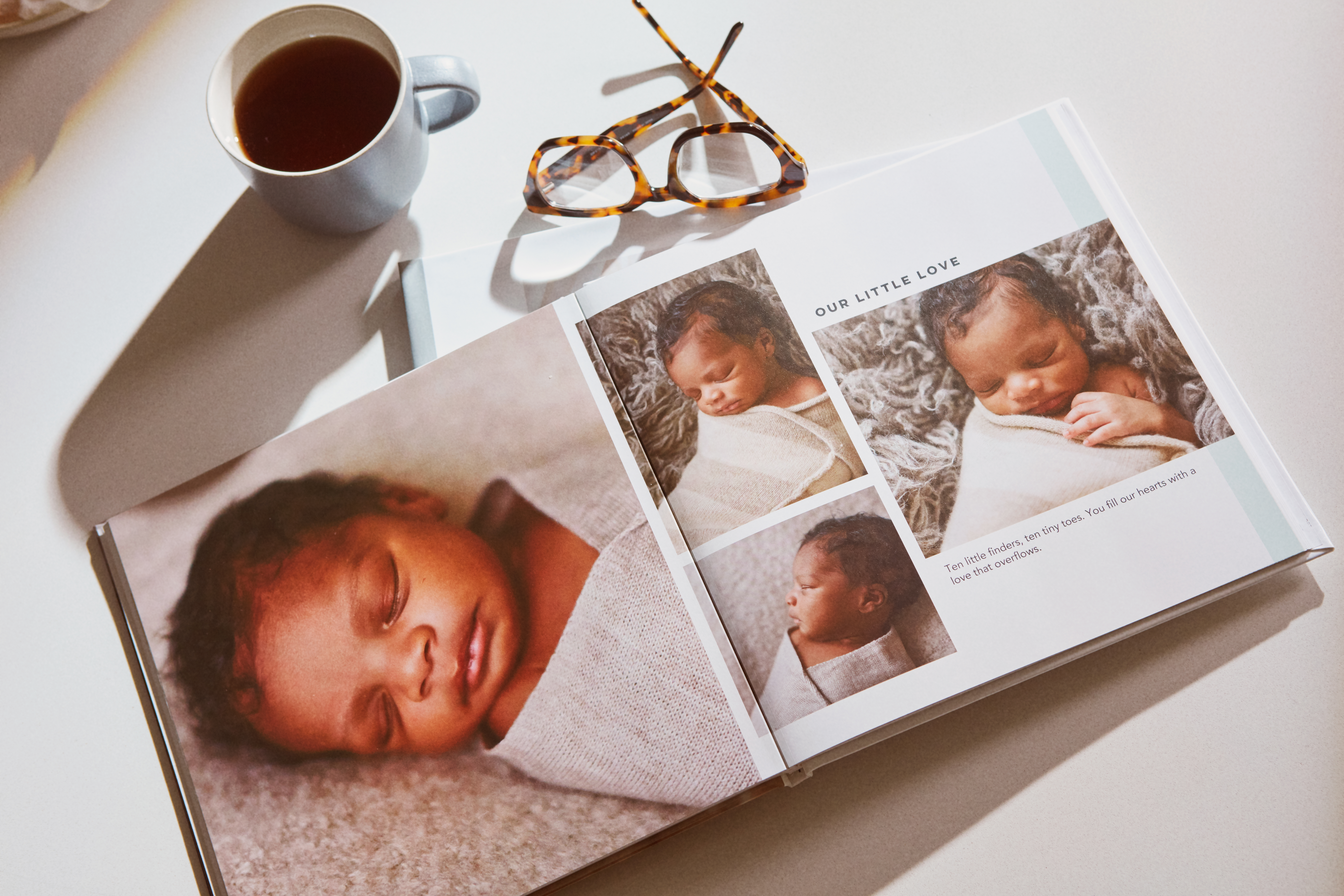 A baby photo book with a collage of baby photos next to glasses and a cup of coffee