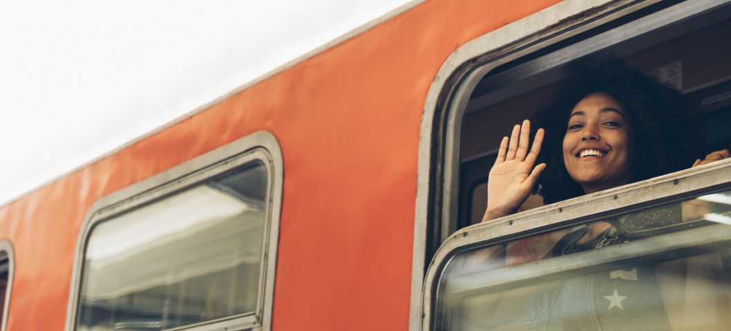 Smiling woman waving hand through train window.