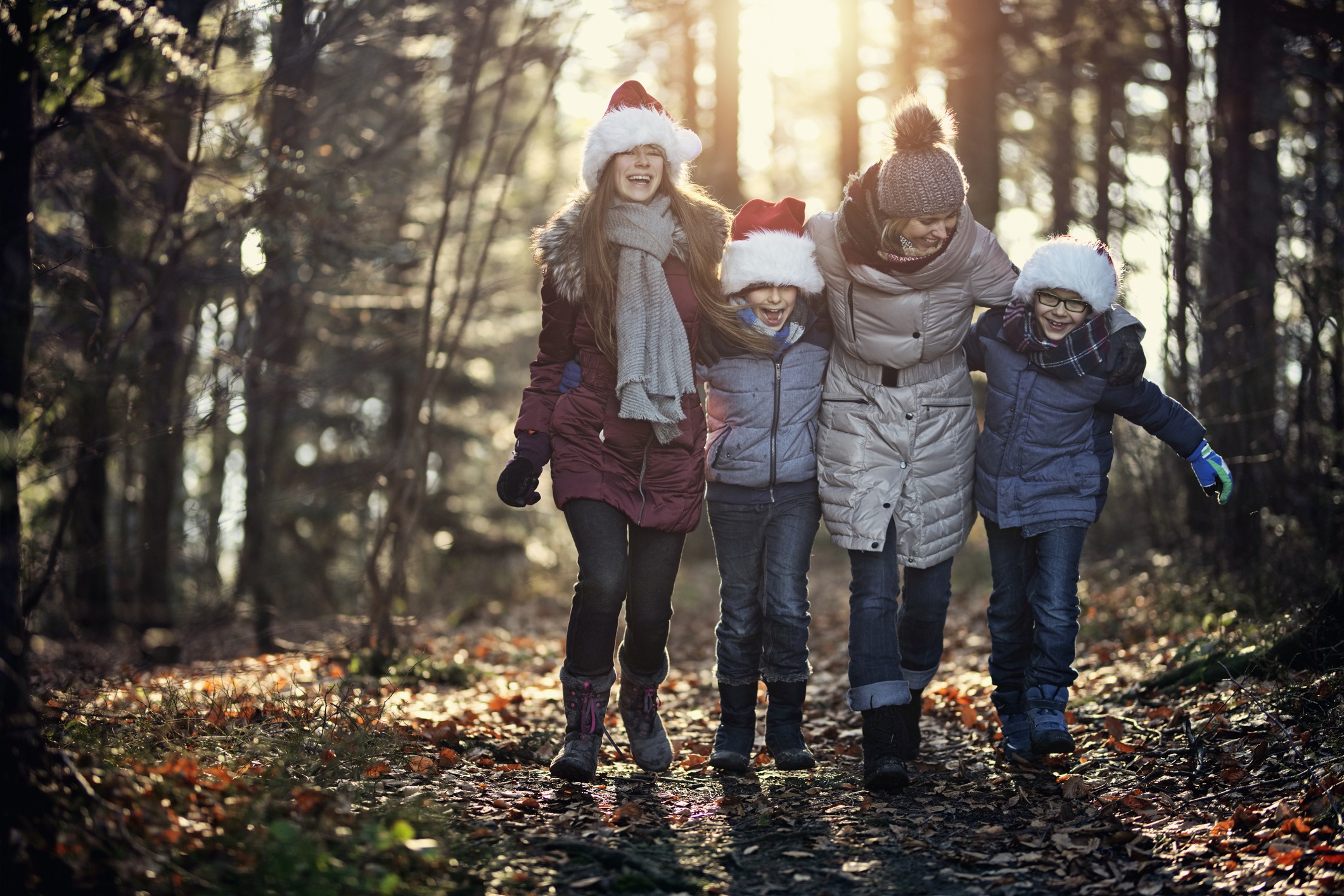 Mother with kids walking in forest. The kids are wearing Santa's caps.