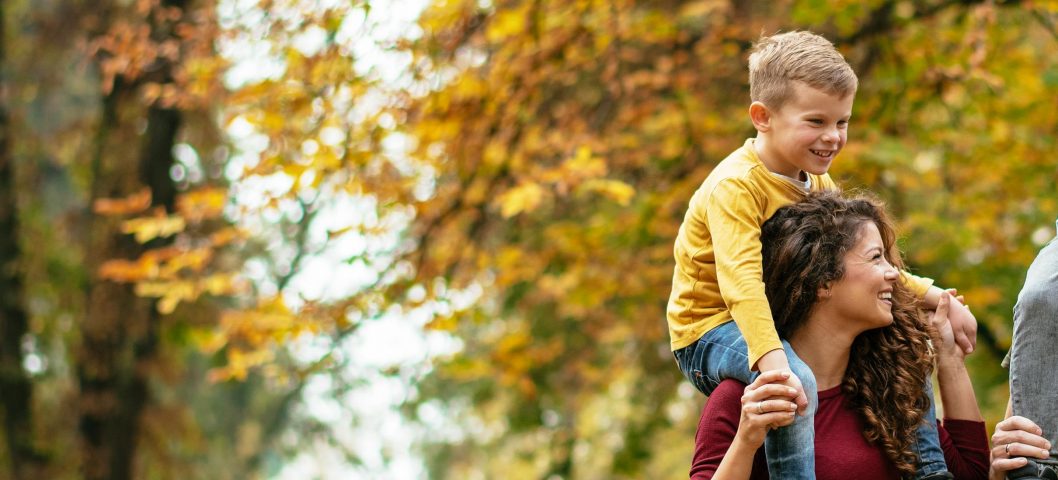 Kids on their parent's shoulders walking in the park.