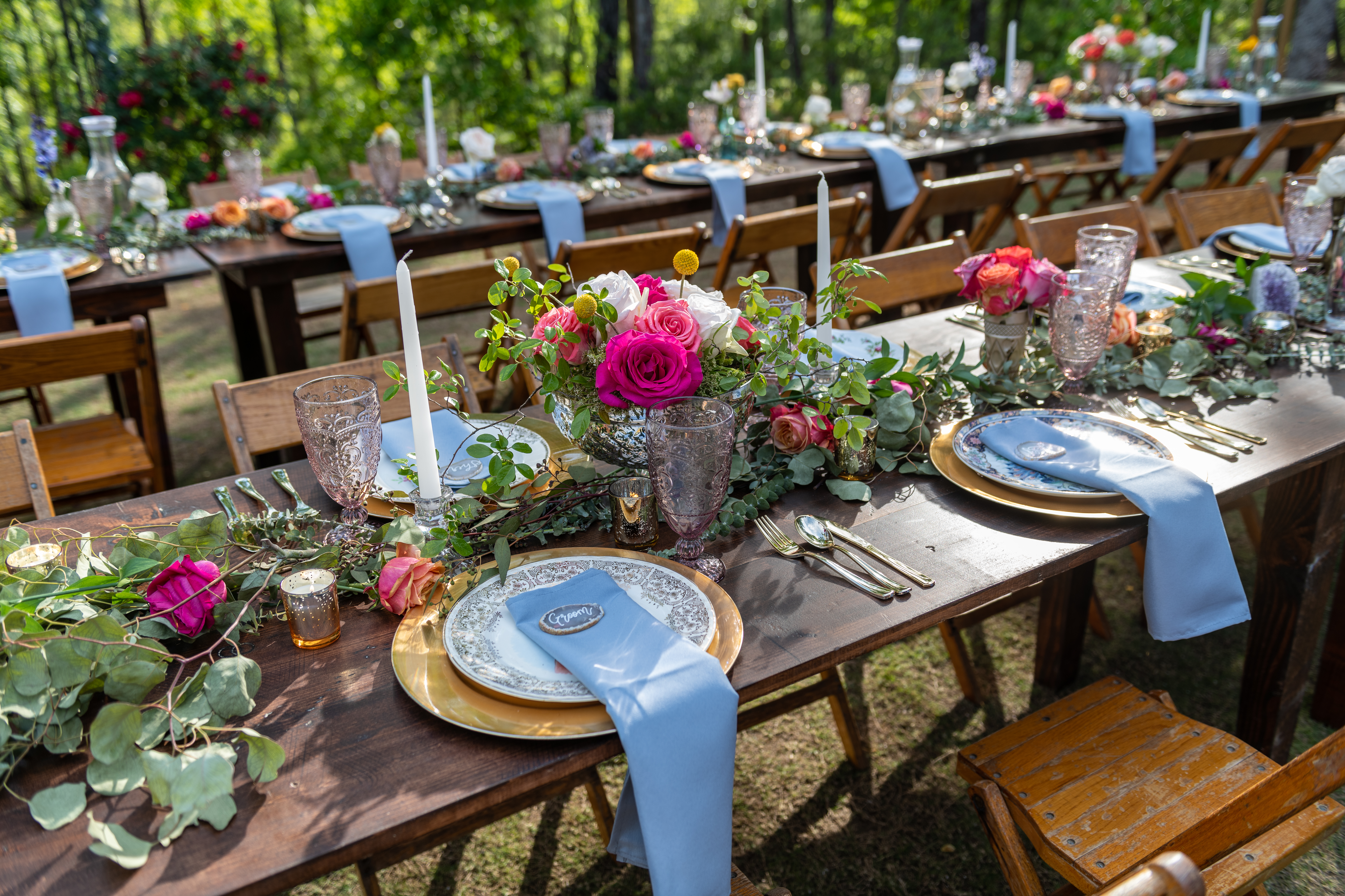 Outdoor wedding place settings for bride and groom at picnic table. Rustic farmhouse flair with roses and vintage mismatched plates