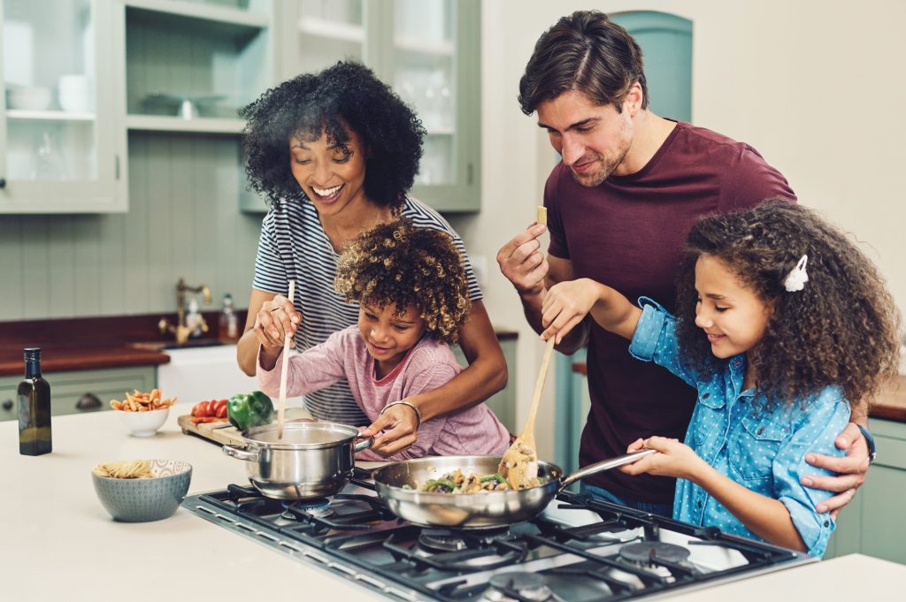 Family of four cooking together in their kitchen at home