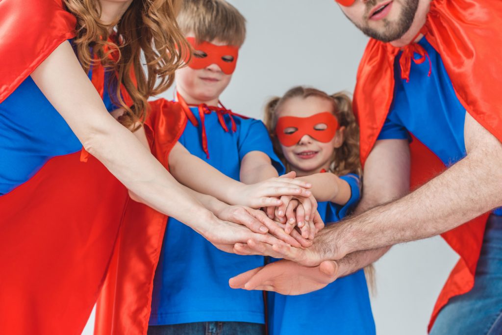 cropped shot of super family in costumes stacking hands together