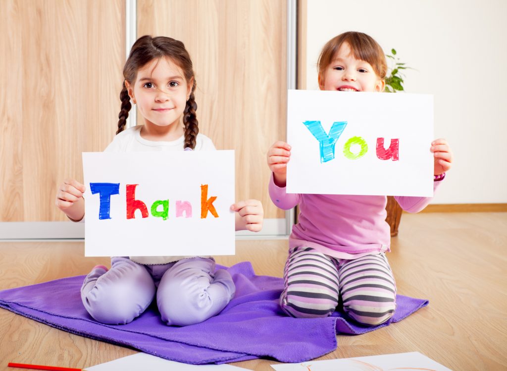 two girls holding up thank you card drawings