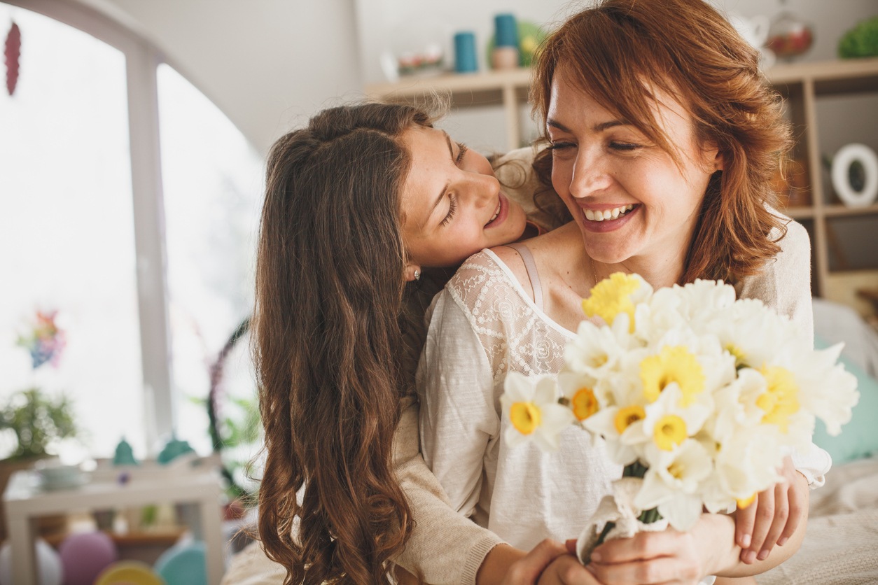Girl is giving a bouquet of fresh daffodils to her mother at home