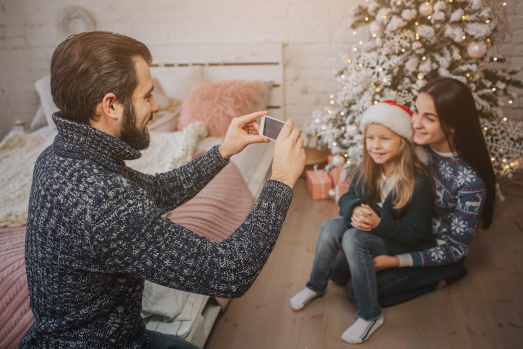Smiling young family in Christmas atmosphere making photo with smartphone