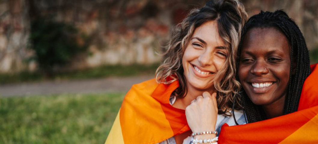 two woman sitting on the grass with a pride flag around them