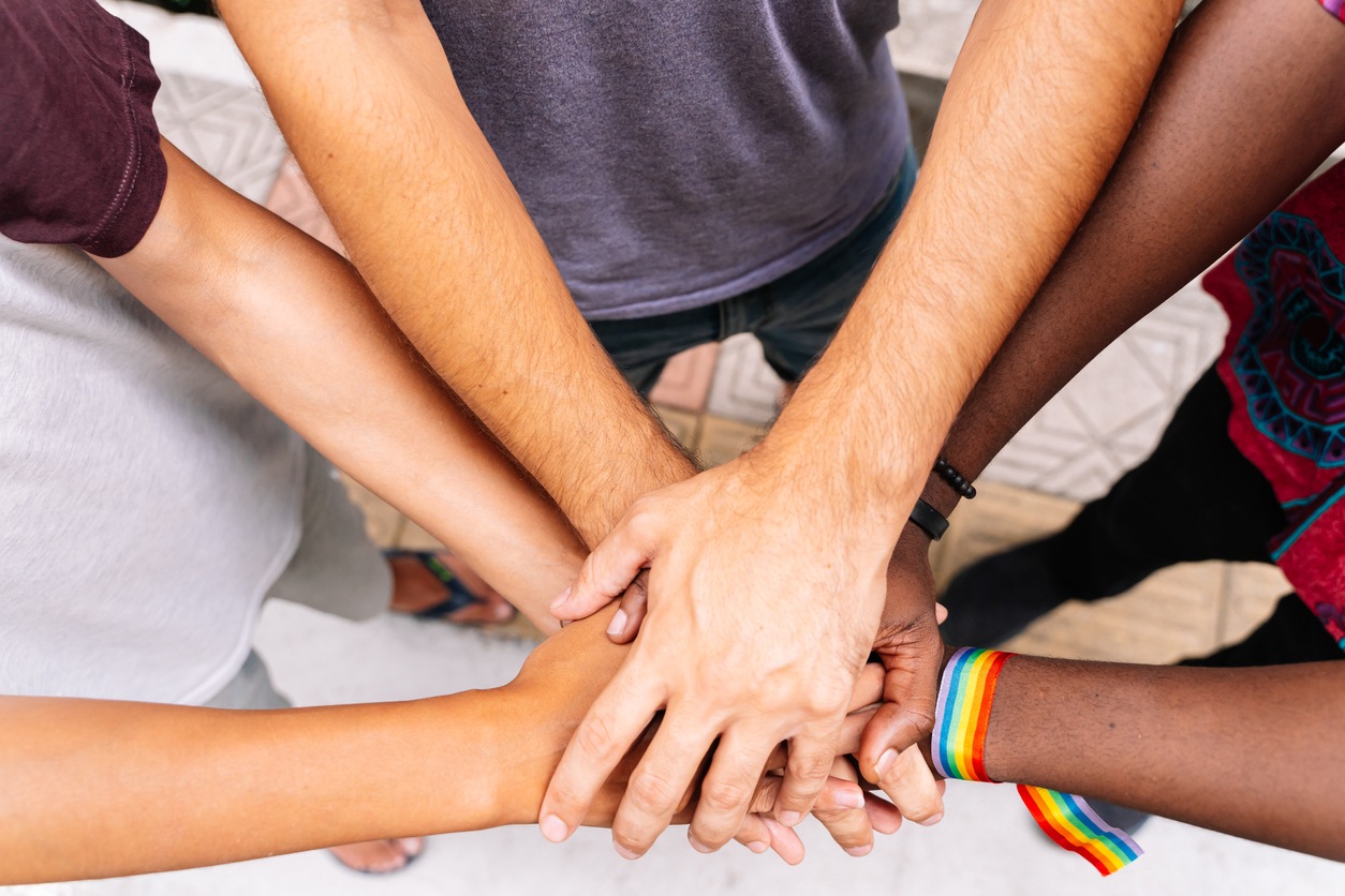 Hands of a group of people of different ethnicities with an LGBTQ+ flag bracelet