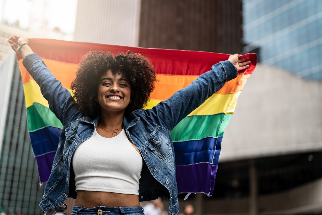 Young woman holding up a pride parade flag with beautiful rainbow colors in support of the LGBTQ+ community
