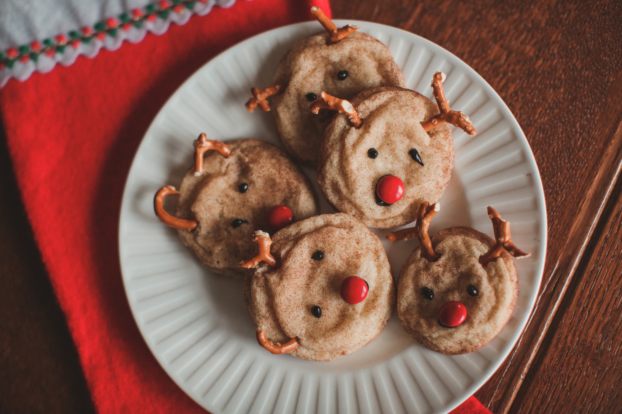 Home made reindeer Christmas cookies with little red candy noses sit on a white plate ready for a holiday celebration.