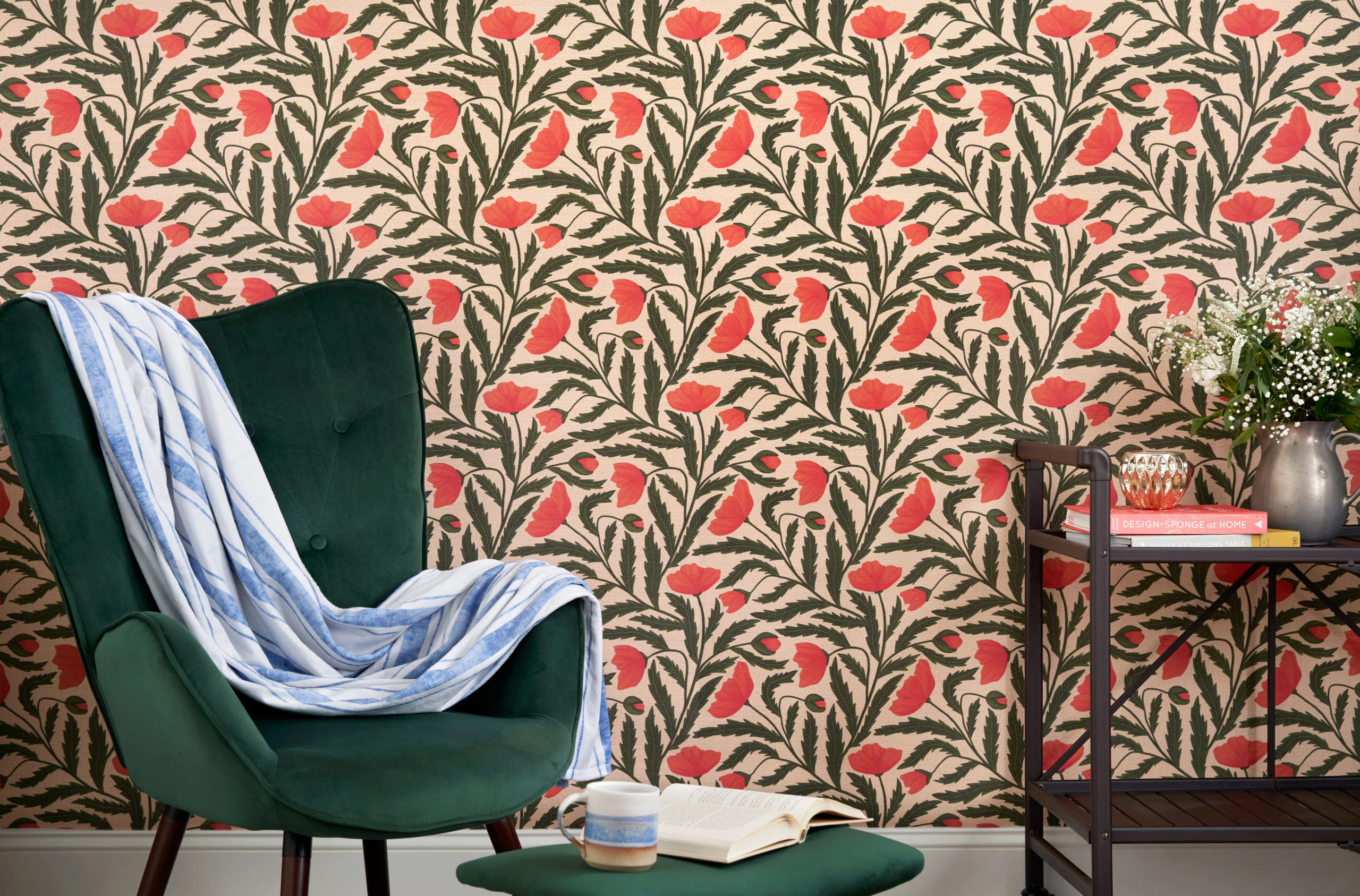 Red and green floral wallpaper featuring a dark green chair and silver flower pitcher