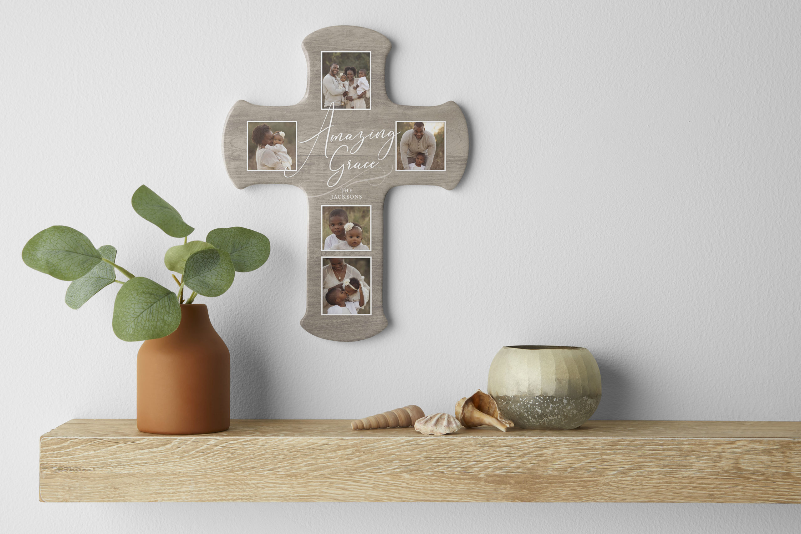 Amazing grace wall cross mounted above a wooden shelf featuring a plant seashells and a small vase