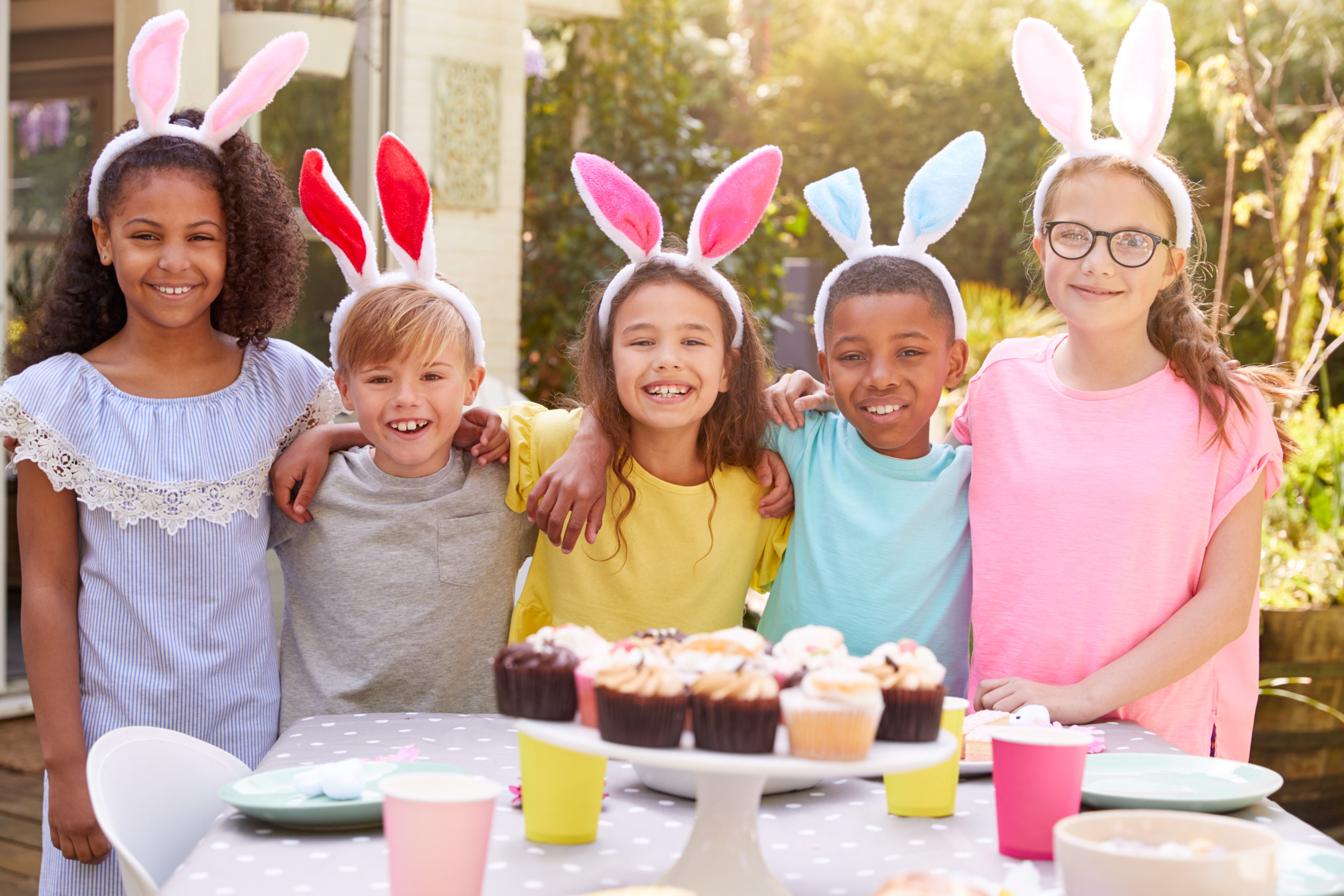 Portrait Of Children Wearing Bunny Ears Enjoying Outdoor Easter Party In Garden At Home
