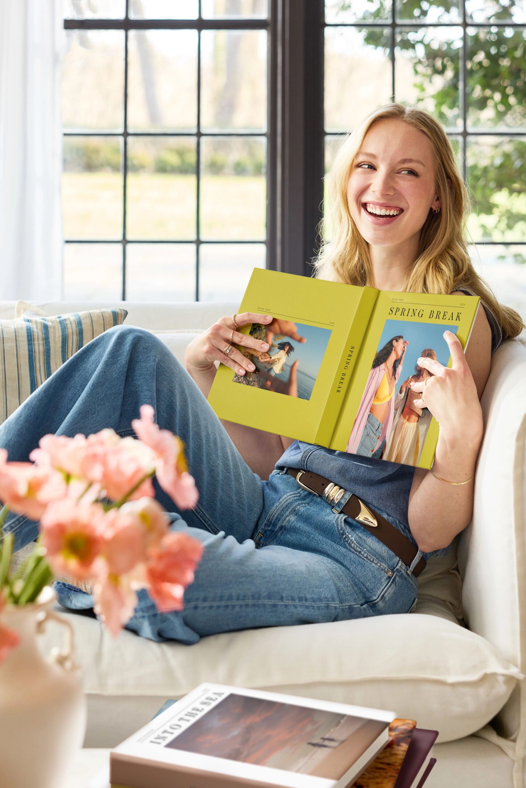 woman sitting on couch looking through photo book with photo books on coffee table