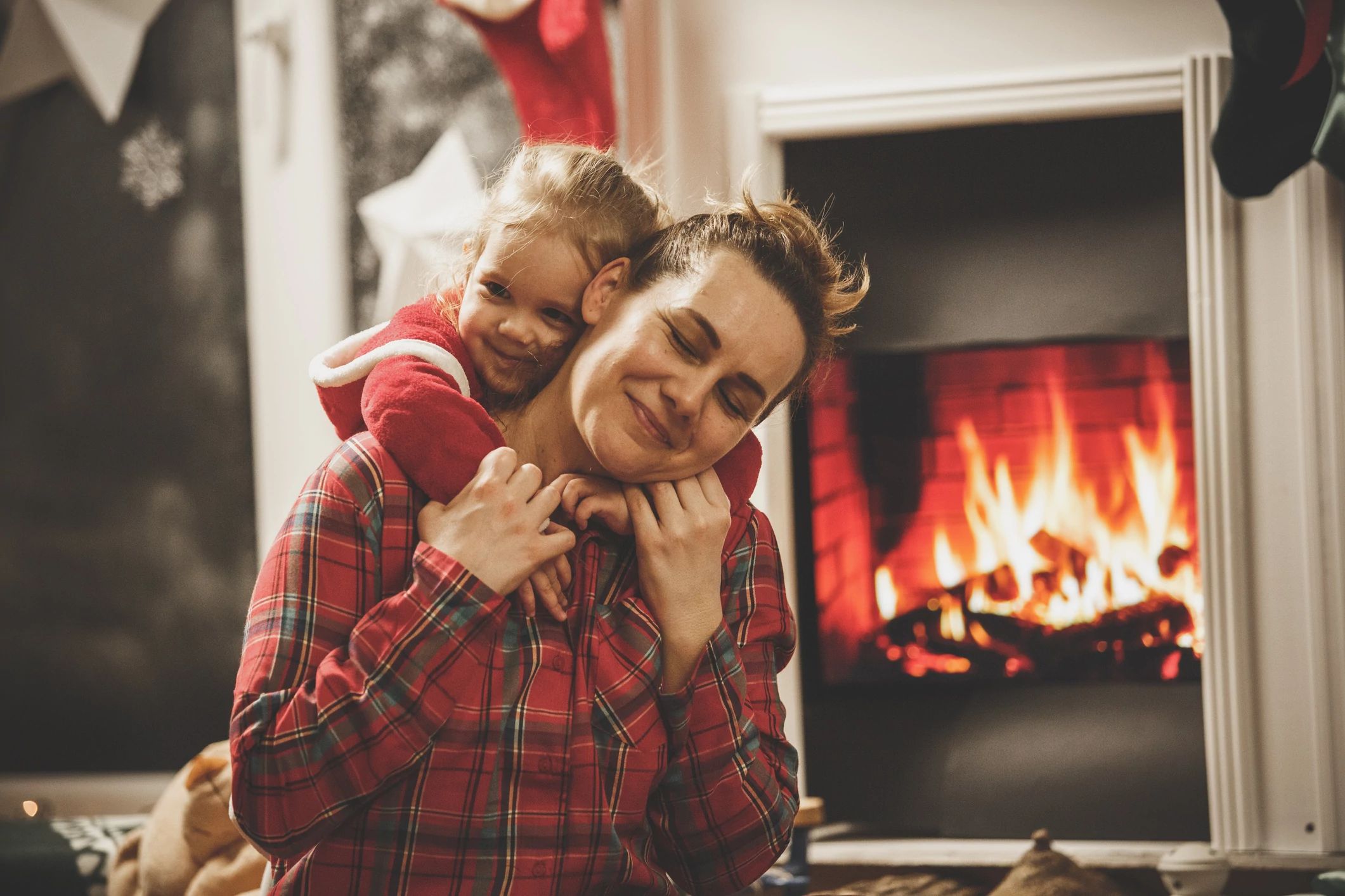 mom and child wearing matching pajamas by the fireplace