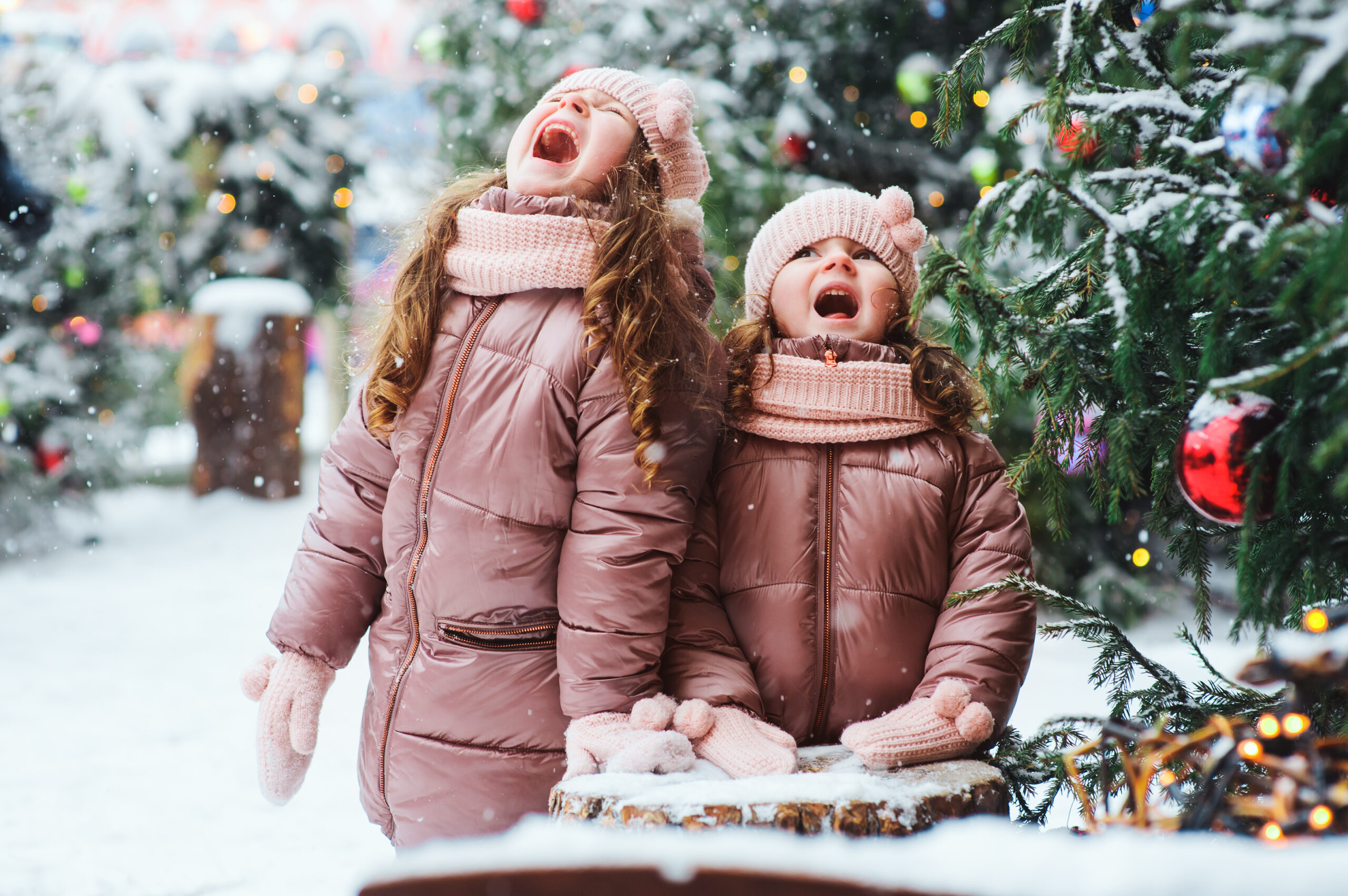 Christmas portrait of two happy sisters playing outdoor in winter snowy city decorated for New Year holidays