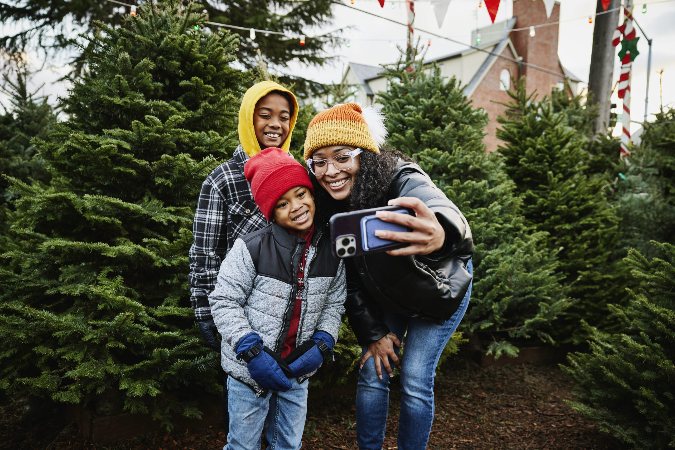 smiling mother and sons taking a selfie while shopping for tree in Christmas tree lot