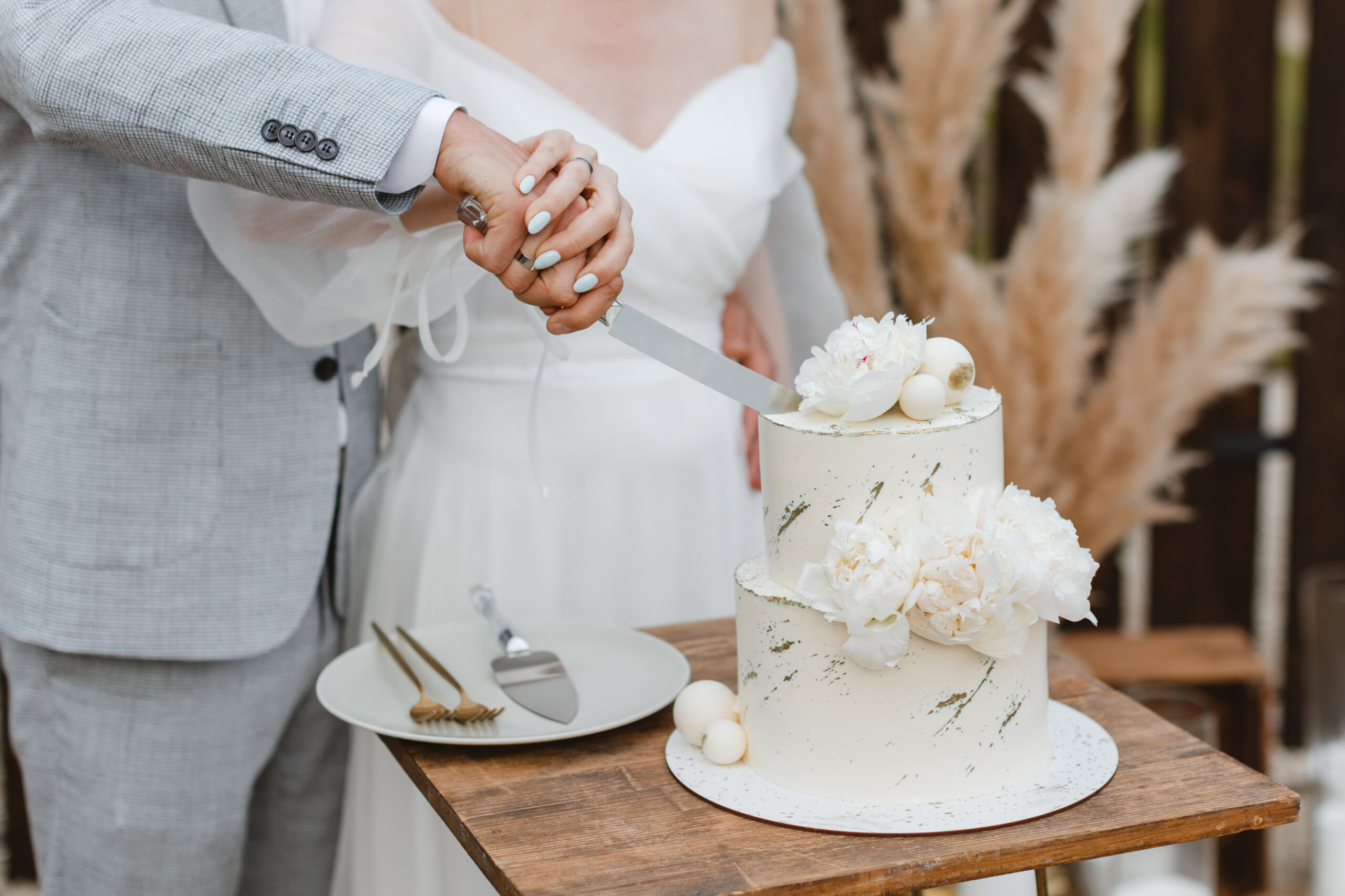 Bride and a groom is cutting their beautiful wedding cake on wedding banquet. Hands cut the cake with delicate white flowers.