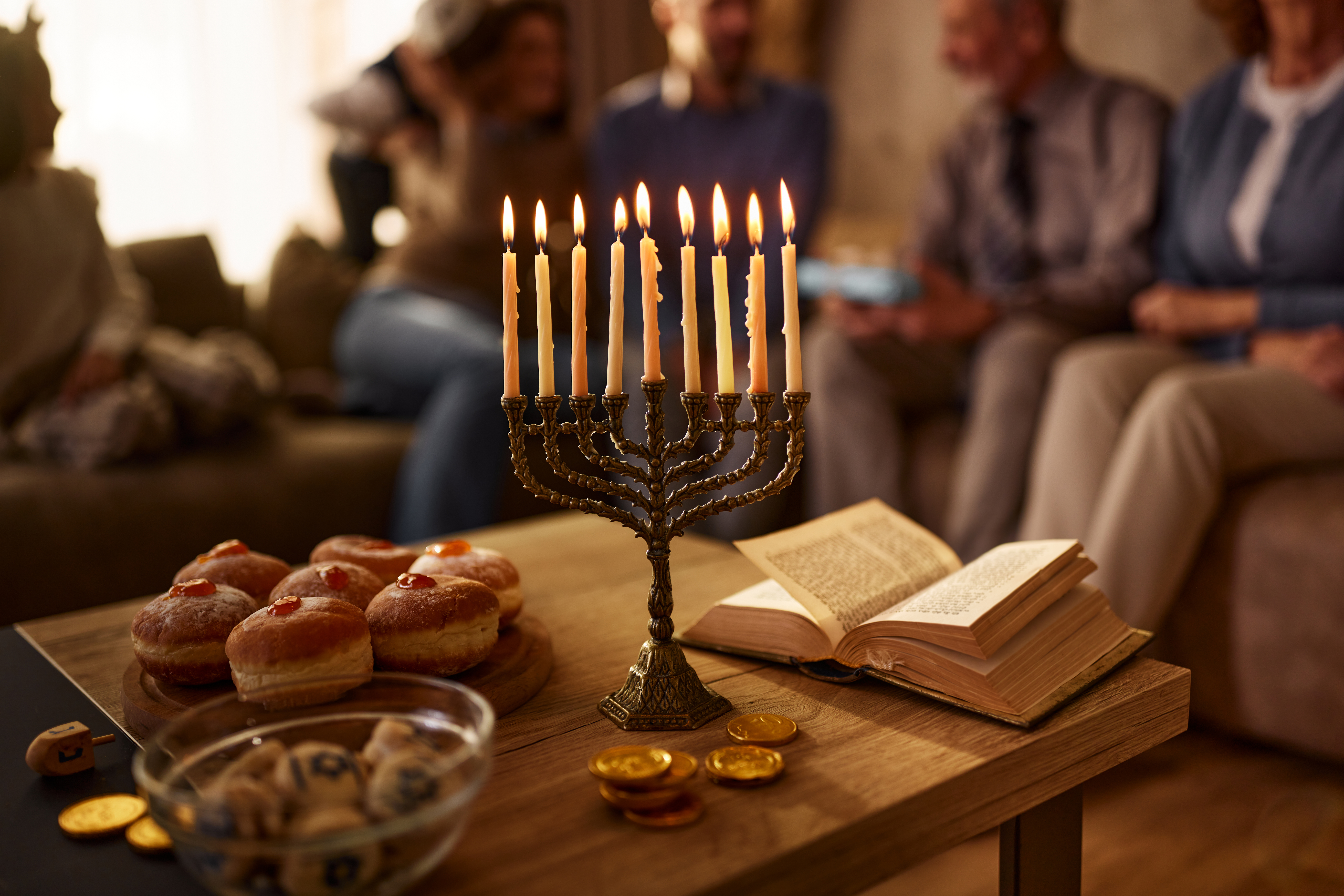 Close up of menorah with traditional food and Torah for Hanukkah with extended family in the background.