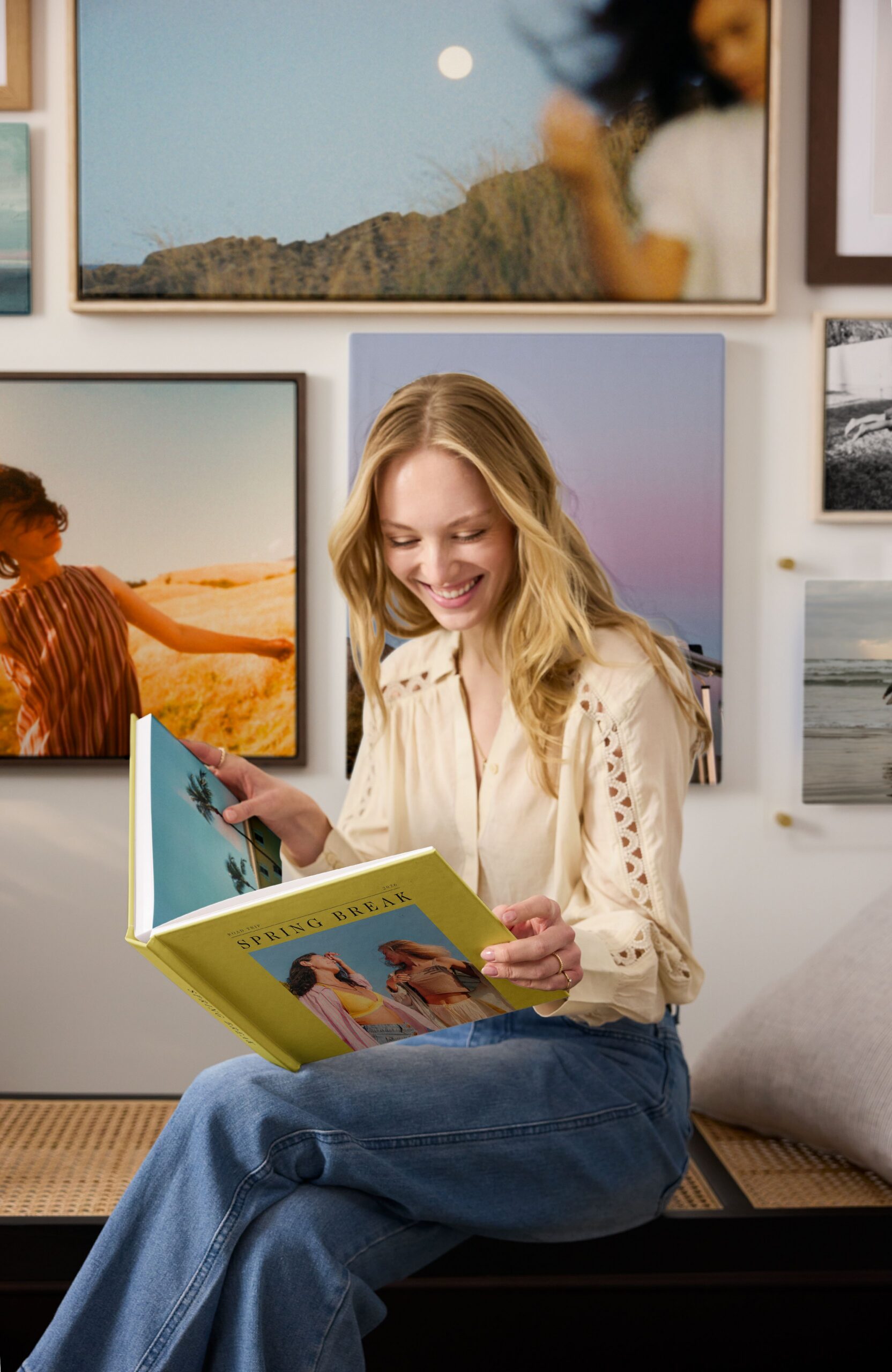 woman holding travel photo book in front of gallery wall of travel photos
