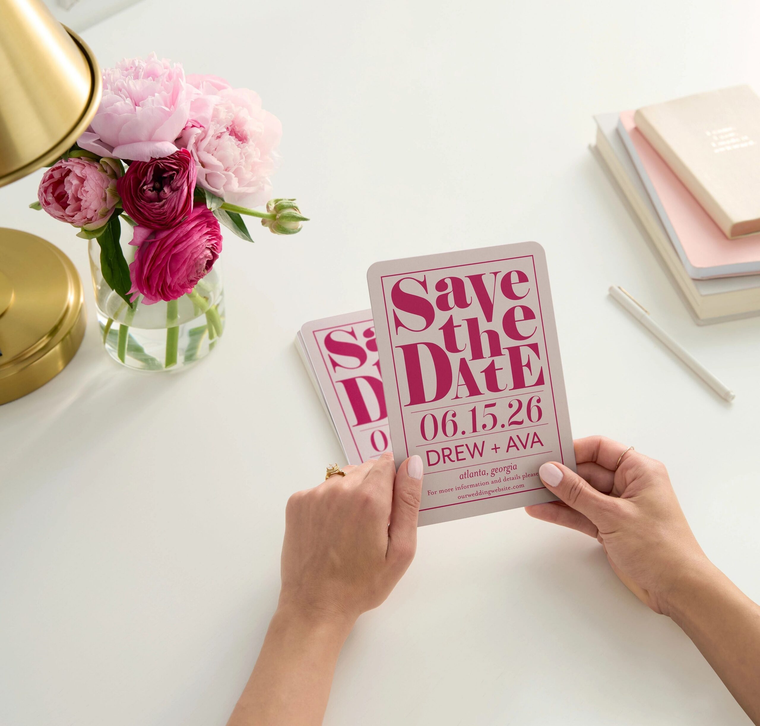 hands holding a pink save the date card on a desktop